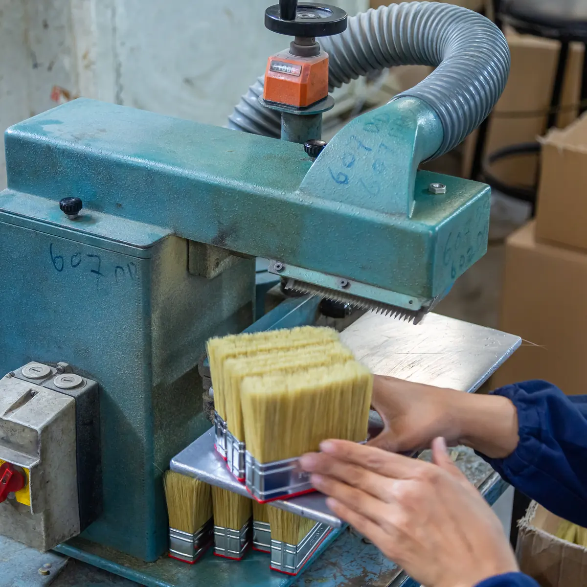A PETA worker pressing a block of finished paint brushes into the trimming head